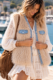Gilet sans manches en fausse fourrure à col châle Gilets et vestes sans manches Femme bohème chic Gilet sans manches en fausse fourrure écrue avec poches et finitions en jean bleu, porté sur une robe bohème blanche.